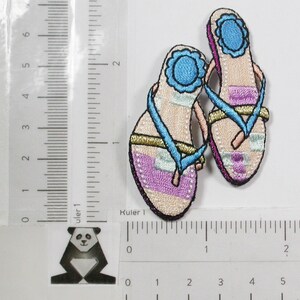 May include: Two embroidered iron-on patches of pink and blue flip flops with gold accents. The patches are approximately 2 inches long.