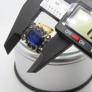Puede incluir: Un anillo de oro con una piedra preciosa azul y un borde de pequeñas piedras azules. El anillo se está midiendo con un calibre digital que muestra 1,98 mm.