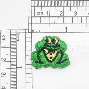 May include: Green embroidered frog patch with a yellow and black bow tie. The frog is approximately 1 inch wide.