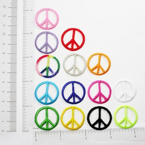 May include: A collection of embroidered peace sign patches in various colors, including pink, red, purple, green, silver, orange, blue, and black. Each patch is a circular design with a peace symbol in the center. The patches are arranged on a white surface.