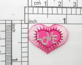 May include: Pink felt heart-shaped patch with white stitching and silver glitter lettering that reads "LOVE".