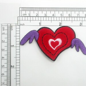 May include: Red felt heart with a white heart inside, with purple wings on either side. The heart is about 2 inches wide.