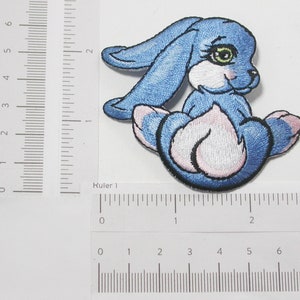May include: Blue embroidered iron-on patch of a cartoon bunny rabbit with white fur and pink accents. The bunny is sitting with its paws tucked under its chin.