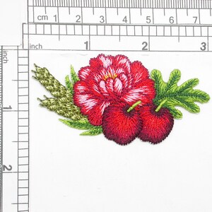 May include: Red embroidered flower with green leaves and two red cherries. The flower has a white center and is surrounded by green leaves.
