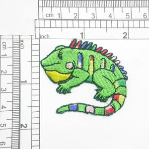 May include: Green embroidered iguana patch with a colourful striped tail and a yellow underside. The patch is approximately 5 cm long.