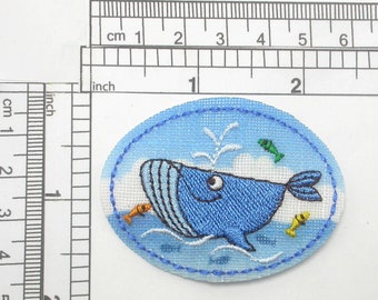May include: A blue whale embroidered patch with a white cloud and orange, yellow, and green fish. The patch is oval shaped and has a blue border.
