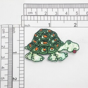 May include: Green and orange embroidered turtle patch with a red mouth. The patch is approximately 5 cm long.