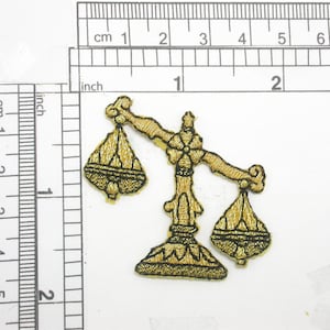 May include: Gold-colored embroidered iron-on patch of a scale with black outlines. The scale is a symbol of justice and law.