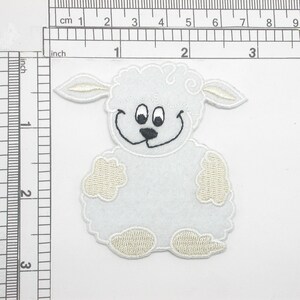 May include: White felt applique of a smiling lamb with black eyes and a black nose. The lamb has a white fluffy body and white fluffy legs.