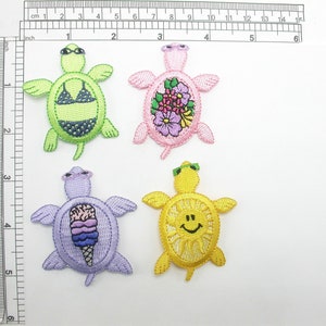May include: Four embroidered iron-on patches of sea turtles. The turtles are green, pink, purple, and yellow. The turtles have different designs, including a swimsuit, flowers, ice cream, and a smiley face.