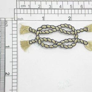 May include: Gold rope trim with a navy blue centre and tassels on each end. The trim is tied in a knot.