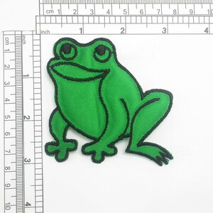 May include: Green felt frog applique patch with black stitching. The frog is sitting with its legs outstretched.
