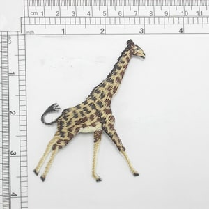 May include: Embroidered iron-on patch of a brown and tan giraffe with a long neck and legs. The giraffe is standing on a white background.