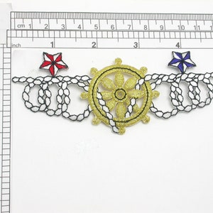 May include: Embroidered nautical applique featuring a gold ship's wheel, black and white rope detailing, and red and blue star accents. The applique measures approximately 5 inches wide.