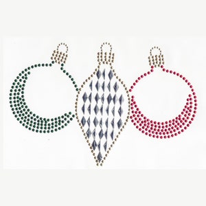 Peut inclure: Trois décorations de Noël en forme de goutte d'eau, faites de strass. La décoration de gauche est verte, celle du centre est argentée et noire, et celle de droite est rouge.