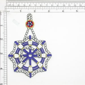May include: A blue and white embroidered patch with a nautical wheel design. The wheel has a blue center and white spokes. The patch is surrounded by a chain design.