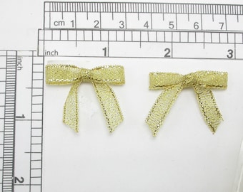 May include: Two gold-colored, metallic, ribbon bows. The bows are approximately 2 inches wide and are made of a shiny, shimmery material.
