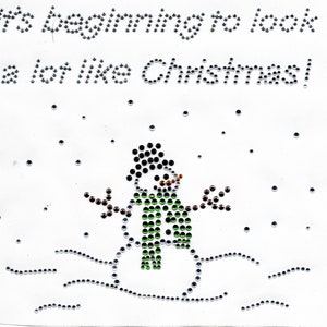 Könnte beinhalten: Es fängt an, nach Weihnachten auszusehen! Ein grüner Schneemann mit einem schwarzen Hut und braunen Zweig-Armen steht in einer verschneiten Szene mit silbernem Glitzer.