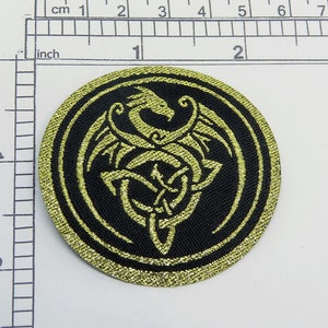 May include: A gold embroidered patch with a black background featuring a stylized dragon design. The dragon is curled around a knot, and the design is surrounded by a gold circle.