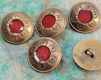 May include: A collection of antique brass buttons with a red center. The buttons have an ornate, embossed design around the perimeter. One button shows the loop on the back. These buttons are ideal for sewing and craft projects.