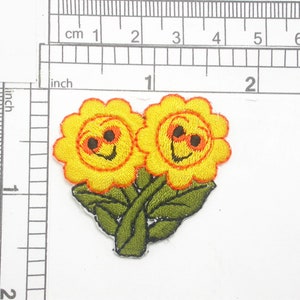May include: Two yellow embroidered flowers with orange centers and smiling faces, with green leaves and stems.