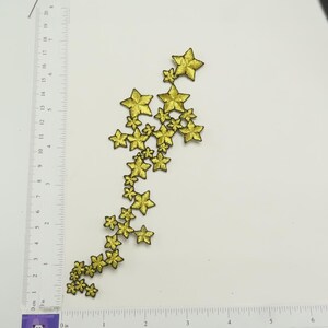 Peut inclure: Un groupe d'étoiles dorées à paillettes avec des contours noirs disposées en cascade. Les étoiles mesurent environ 3,8 cm de long.