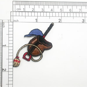 May include: Embroidered patch of a brown leather riding boot with a blue baseball cap and a red and white whip. The boot has a gold buckle and a brown strap.
