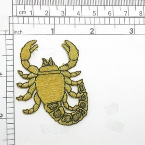 May include: A gold embroidered scorpion patch with black outlines. The scorpion is facing right with its tail curled up.