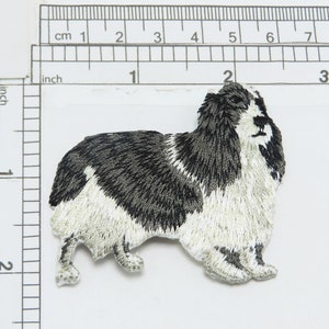 May include: Embroidered iron-on patch of a black and white dog with fluffy fur. The dog is facing right and has its tongue sticking out.