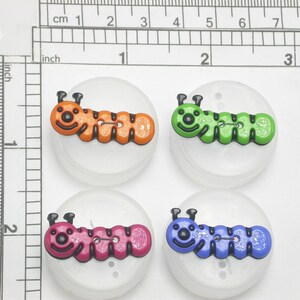 May include: Four colorful caterpillar-shaped buttons. Each button features a different color: orange, green, pink, and blue. The buttons are approximately 1 inch in diameter and are set on white, circular bases.