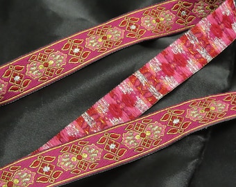 May include: Pink ribbon with gold and red floral embroidery. The ribbon has a repeating pattern of flowers and geometric shapes. The center ribbon has a tie-dye effect with red and silver. The ribbon is likely used for crafting or embellishment.
