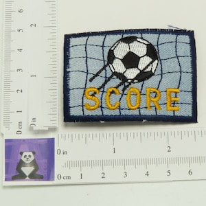 May include: An embroidered patch with a blue background and a white football going into a net. The word "SCORE" is embroidered in yellow letters.