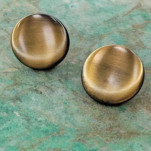 May include: A pair of round, gold-toned earrings with a brushed finish. The earrings are slightly domed and have a smooth, polished surface.