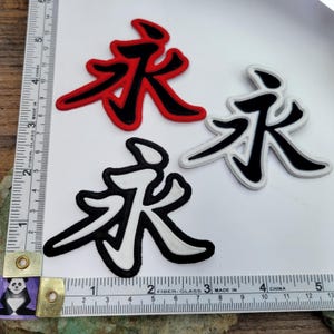 Op de afbeelding: Drie strijkbare patches met het Chinese karakter "永" (Yong) in verschillende kleuren. De patches zijn rood met zwarte omtrek, zwart met witte omtrek en wit met zwarte omtrek. De patches zijn ongeveer 5 cm groot.