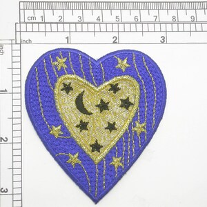 Pode incluir: Um remendo azul em forma de coração com um coração dourado dentro. O coração dourado tem uma lua crescente e estrelas dentro. O remendo tem cerca de 5 cm de largura.