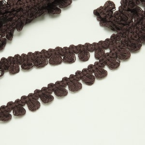 May include: Brown crocheted trim with a scalloped edge and small pom-poms.