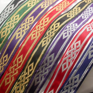 Może przedstawiać: Kolekcja kolorowych wstążek z celtyckim wzorem węzła. Wstążki są w różnych kolorach, w tym czarnym, zielonym, fioletowym, czerwonym i niebieskim, z metalicznymi złotymi lub srebrnymi akcentami. Wstążki są ułożone po przekątnej.