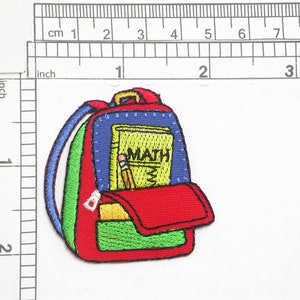 May include: Embroidered iron-on patch of a red backpack with a blue, green, and white striped strap. The backpack has a yellow pocket with the word "MATH" on it and a pencil sticking out.