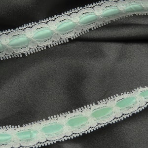 May include: White lace trim with a light blue satin ribbon. The trim has a scalloped edge and is perfect for adding a touch of elegance to any project.