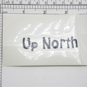 Puede incluir: Una pegatina blanca con el texto "Up North" impreso en negro.