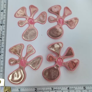 Pode incluir: Quatro patches termocolantes em forma de flor rosa e dourado. Cada patch tem um centro rosa e um acabamento metálico dourado.
