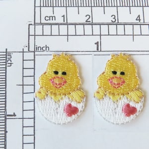 Pode incluir: Dois apliques bordados de pintinhos amarelos, cada um com um coração rosa em uma casca de ovo branca. Os apliques medem aproximadamente 2,5 cm de diâmetro.