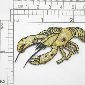 May include: Gold embroidered iron-on patch of a crayfish, approximately 5 cm long.