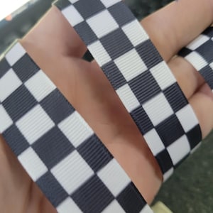 May include: Close-up of a black and white checkered ribbon. The ribbon has a repeating pattern of black and white squares. The ribbon is made of a textured material.