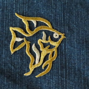 May include: A gold embroidered patch of a stylized fish design on a blue denim background.