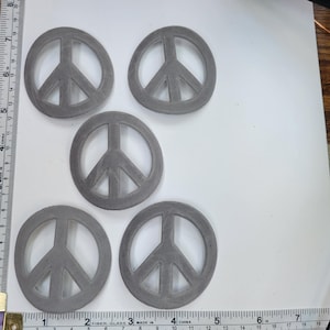 Peut inclure: Cinq découpes de signe de paix grises, chacune d'environ 7,5 cm de diamètre, sur un fond blanc.