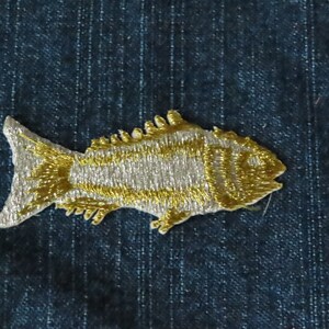 May include: Embroidered fish patch in gold and silver thread, set on a dark blue denim background. The patch showcases a detailed design of scales and fins. Ideal for customising clothing or accessories.