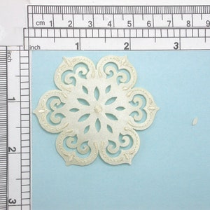 May include: A white, decorative, lace snowflake with intricate cutouts. The snowflake is approximately 2 inches in diameter.