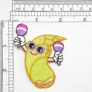 May include: Yellow cartoon banana character with a smiling face wearing sunglasses and holding two maracas. The maracas are purple and pink.