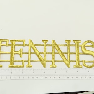 May include: Gold embroidered iron-on patch with the word "TENNIS" in a decorative font.